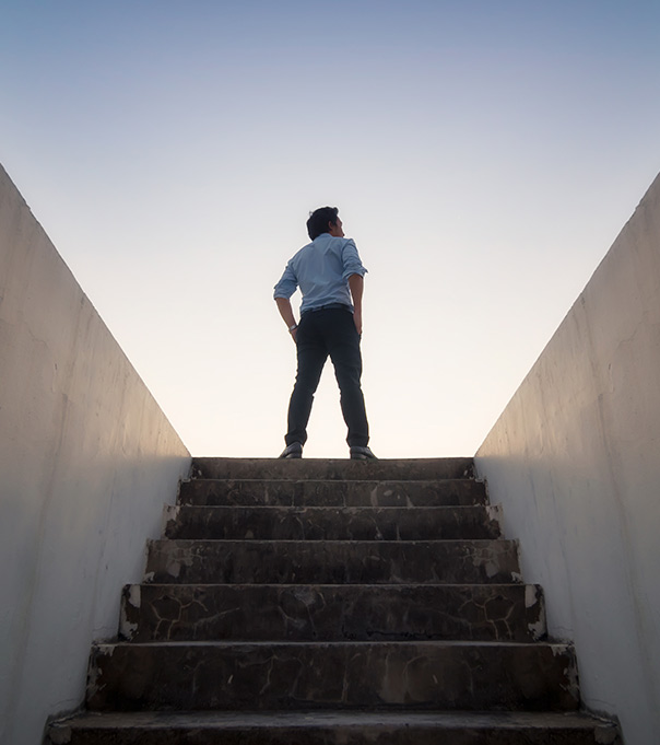 A man stands at the top of a stairwell, looking at the sky. This represents how online Jungian Therapy in San Francisco and Los Angeles can help you get to the source of your mental health issues or life problem.